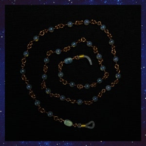 Könnte beinhalten: Eine blaue und goldene Brillenkette mit schillernden Perlen. Die Kette hat zwei Verschlüsse zum Befestigen an Brillen.