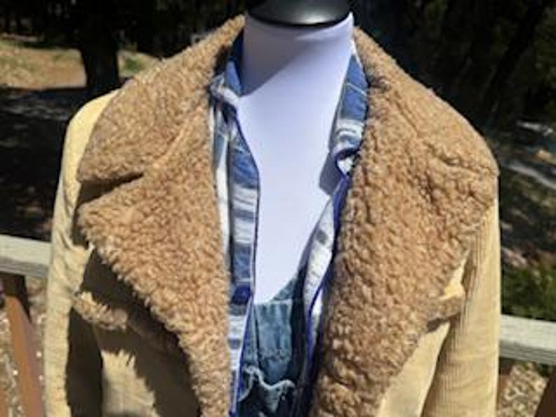 May include: A tan corduroy jacket with a brown faux fur collar and lining. The jacket is worn over a blue and white plaid shirt and denim overalls. The jacket has a classic, vintage style.