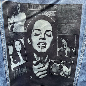 Può includere: Giacca di jeans blu con grafica in bianco e nero sul retro. La grafica presenta una donna con una sigaretta e la scritta "ULTRAVIOLENCE", insieme a diverse immagini più piccole e testo.