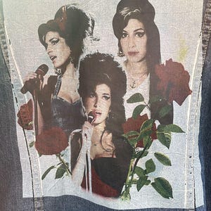May include: A denim jacket with a patch featuring three women with dark hair and red roses. The women are wearing different outfits and have different hairstyles. The patch is on the back of the jacket.