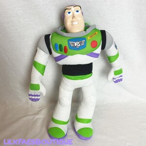 K&ouml;nnte beinhalten: Eine Pl&uuml;schpuppe von Buzz Lightyear, mit einem Plastikkopf und einem Stoffk&ouml;rper. Die Puppe ist haupts&auml;chlich wei&szlig;, gr&uuml;n und lila, mit einem schwarzen Mittelteil. Die Puppe tr&auml;gt das Wort "LIGHTYEAR" auf der Brust und den Text "LILXFAESBOUTIQUE" unten.
