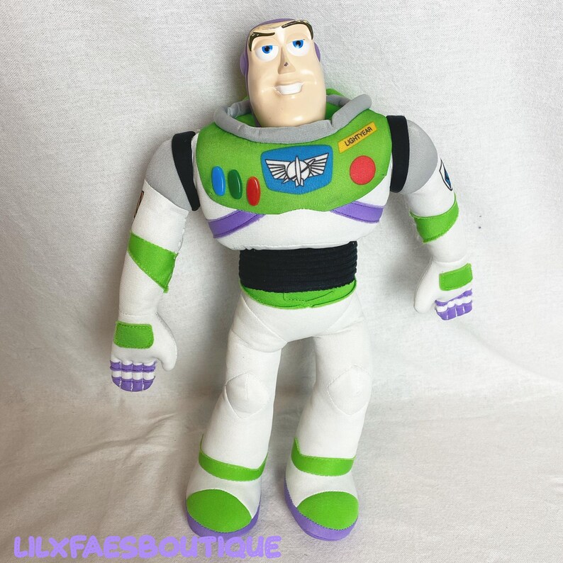 K&ouml;nnte beinhalten: Eine Pl&uuml;schpuppe von Buzz Lightyear, mit einem Plastikkopf und einem Stoffk&ouml;rper. Die Puppe ist haupts&auml;chlich wei&szlig;, gr&uuml;n und lila, mit einem schwarzen Mittelteil. Die Puppe tr&auml;gt das Wort "LIGHTYEAR" auf der Brust und den Text "LILXFAESBOUTIQUE" unten.