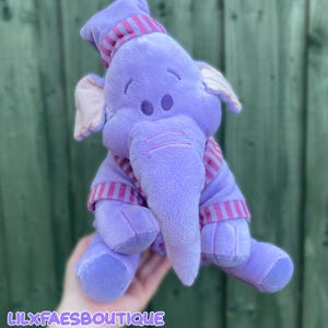 May include: A plush purple elephant toy wearing a matching purple and pink striped nightcap and pajamas. The elephant has soft fabric, embroidered eyes, and light pink inner ears. The text LILXFAESBOUTIQUE is printed in white at the bottom.