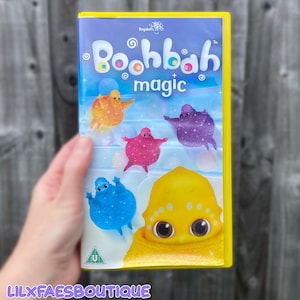 May include: A yellow-cased Boohbah Magic DVD featuring a blue, orange, purple, pink, and yellow character on the cover. The title Boohbah magic is printed in white text at the top. A green U rating symbol is visible in the bottom left corner.