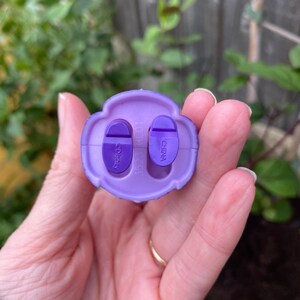 Puede incluir: Una base de pl&aacute;stico morado claro con dos soportes ovalados para los pies en color morado oscuro. La base presenta el texto en relieve Disney en el soporte izquierdo y China en el derecho, con n&uacute;meros moldeados visibles en el centro.