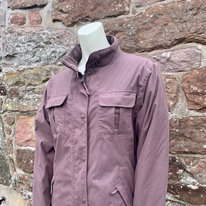 May include: A mauve-colored jacket with a zipper and button closure. The jacket has two large flap pockets on the front and a smaller pocket on the left sleeve.