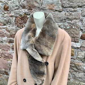 May include: A beige double-breasted coat with a large brown fur collar. The collar is folded over and the fur is visible on both sides.
