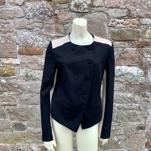 Puede incluir: Una chaqueta negra con cierre de doble botonadura y ribete de color rosa claro en contraste en las mangas y los hombros.