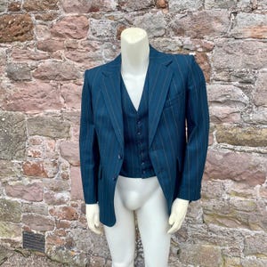 May include: Teal pinstripe suit set, including a blazer and vest, displayed on a mannequin. The suit features a classic design with a notched lapel on the blazer and a button-down vest. The pinstripes are a lighter shade, creating a subtle contrast against the teal fabric.