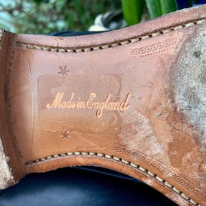 May include: Close-up of the sole of a leather shoe. The sole is a light brown color with visible stitching around the edges. The words "Made in England" are embossed on the sole.