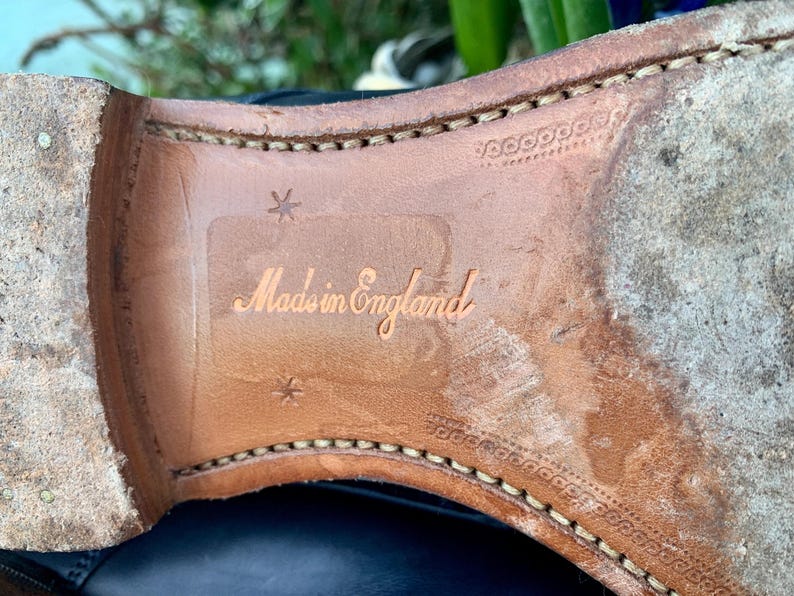 May include: Close-up of the sole of a leather shoe. The sole is a light brown color with visible stitching around the edges. The words "Made in England" are embossed on the sole.