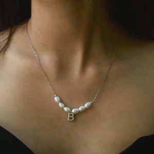 May include: A silver chain necklace with a small letter 'B' charm and a row of white pearl beads.