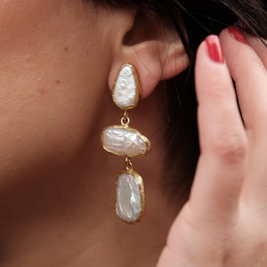 May include: Gold earrings with three white pearl-like drops.