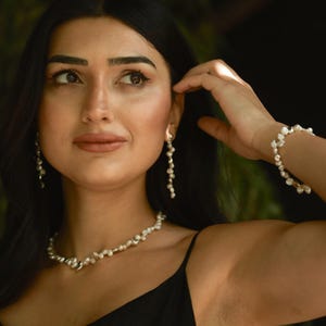 A woman elegantly wearing a handmade keshi pearl jewelry set, including a pearl necklace, drop earrings, and a matching bracelet. The irregularly shaped freshwater pearls are accented with delicate silver details, creating a sophisticated and timeless bridal or special occasion look.