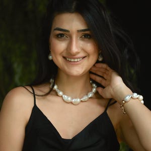 A woman is wearing a coordinated jewelry set composed of large baroque pearls, including a necklace, bracelet, and drop earrings. Each piece highlights the unique, organic shapes of the pearls, creating a naturally elegant look.