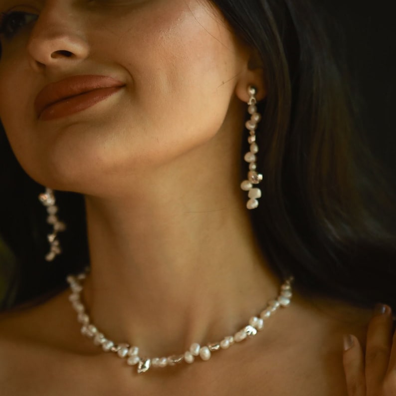 A woman with a soft smile wearing a sterling silver keshi pearl jewelry set, featuring a delicate necklace and long drop earrings.