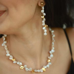 A woman wearing a handmade keshi pearl jewelry set, featuring a long dangling pearl earring and a matching necklace accented with gold-plated keshi pearls. The organic pearl shapes add a modern yet timeless elegance, perfect for bridal or formal occasions.