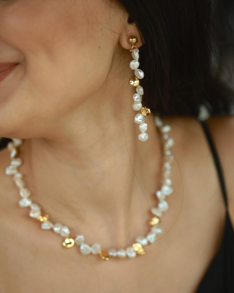 A woman wearing a handmade keshi pearl jewelry set, featuring a long dangling pearl earring and a matching necklace accented with gold-plated keshi pearls. The organic pearl shapes add a modern yet timeless elegance, perfect for bridal or formal occasions.