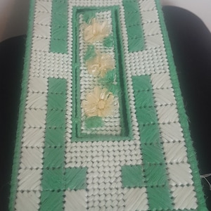May include: A green and white crocheted tissue box cover with a floral design. The cover has a rectangular opening for the tissues.