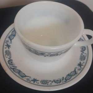 Könnte beinhalten: Ein weißes Tee-Set mit Untertasse mit einem blauen und grünen Blumenmuster. Tasse und Untertasse sind beide aus weißer Keramik.