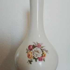 May include: A white ceramic vase with a bulbous base and a slender neck. The vase is decorated with a floral bouquet in shades of pink, yellow, and white. The vase is approximately 25 cm tall.