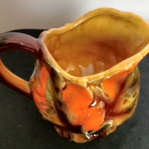May include: A brown ceramic jug with a handle and orange and brown floral design.