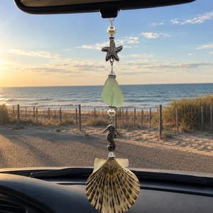 May include: A hanging car ornament featuring a silver-toned starfish charm, a smooth light green sea glass piece, a silver-toned seahorse charm, and a large fan-shaped seashell, all connected by white pearl beads and clear crystal spacers.