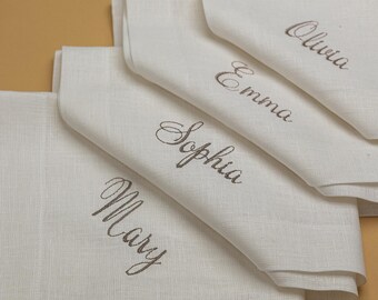Puede incluir: Cuatro servilletas de lino blanco con nombres bordados: Mary, Sophia, Emma y Olivia.
