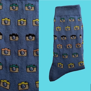 Op de afbeelding: Blauwe sokken met een patroon van kleurrijke camera's. De sokken zijn gemaakt van een zacht, comfortabel materiaal en zijn perfect voor dagelijks gebruik.