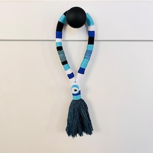 Könnte beinhalten: Ein blauer, weißer und schwarzer Quaste mit einem blauen bösen Auge, das an einem Knopf hängt.