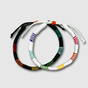 May include: Two colourful friendship bracelets with white, black, orange, yellow, green, blue and purple stripes.