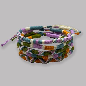 Può includere: Set di quattro braccialetti dell'amicizia colorati con un design intrecciato in tonalità di verde, arancione, bianco e viola.