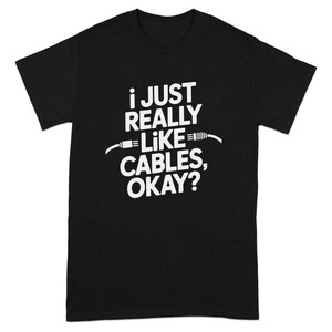 May include: Black t-shirt with white text: "I JUST REALLY LIKE CABLES, OKAY?" The text is centered and features a cable graphic. The shirt is a short-sleeved crew neck.