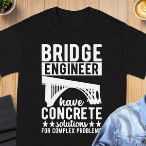 May include: A black short-sleeve t-shirt featuring white text that reads BRIDGE ENGINEER have CONCRETE solutions FOR COMPLEX PROBLEMS, accompanied by a graphic illustration of an arched bridge positioned between the lines of text.
