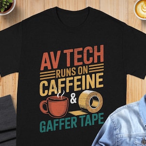 May include: Black t-shirt with a graphic design. The design features the text "AV TECH RUNS ON CAFFEINE & GAFFER TAPE" in orange, yellow, and teal. A coffee cup and roll of tape are also included in the design.