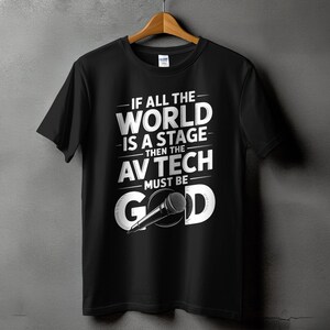 May include: Black t-shirt with the text "IF ALL THE WORLD IS A STAGE THEN THE AV TECH MUST BE GOOD" in white. A microphone graphic is included in the design. The shirt is hanging on a wooden hanger.