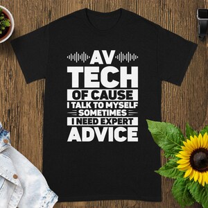 May include: Black t-shirt with white text that reads "AV TECH OF COURSE I TALK TO MYSELF SOMETIMES I NEED EXPERT ADVICE". The shirt is displayed on a wooden surface with a sunflower and a small potted plant.