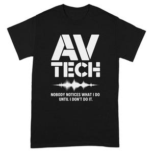 May include: Black t-shirt with white text and a sound wave graphic. The text reads "AV TECH" above a sound wave, with the phrase "NOBODY NOTICES WHAT I DO UNTIL I DON'T DO IT" below. A casual tee.