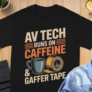 May include: Black t-shirt with the text "AV TECH RUNS ON CAFFEINE & GAFFER TAPE". The design includes a blue coffee cup and a roll of tape in orange and yellow.
