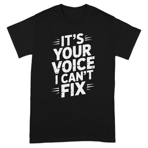 May include: Black t-shirt with the white text "IT'S YOUR VOICE I CAN'T FIX". The text is in a bold, distressed font. The shirt has a crew neck and short sleeves.