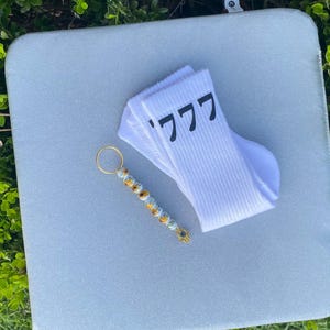May include: A pair of white socks with the number "777" printed on them, a beaded keychain with a gold charm, and a light blue background.