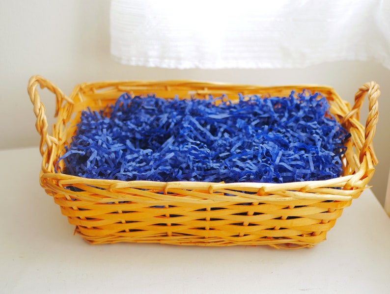 May include: A wicker basket with a woven handle filled with blue shredded paper.