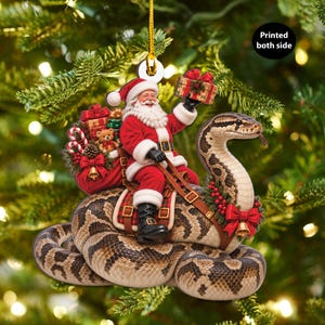 Könnte beinhalten: Ein Weihnachtsschmuck mit dem Weihnachtsmann, der auf einer großen, braun-beige gemusterten Schlange reitet. Der Weihnachtsmann trägt einen roten Anzug, hält ein Geschenk und einen Sack mit Präsenten. Ein Kranz mit roten Beeren und einer goldenen Glocke schmückt die Schlange.
