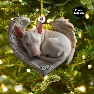 Può includere: Un ornamento a forma di cuore con un Bull Terrier bianco addormentato all'interno di ali d'angelo. Il nome del cane, "Bella", è scritto sull'ornamento. L'ornamento è appeso a un filo d'oro, con il testo "Printed both side".