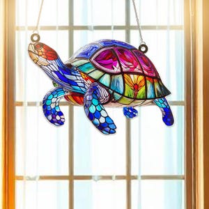 May include: A stained glass turtle suncatcher with a colorful design. The turtle is hanging from a window with a string.