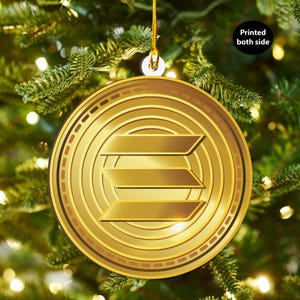May include: Gold-colored Christmas ornament with a stylized letter E in the center. The ornament is round and has a concentric circle design.