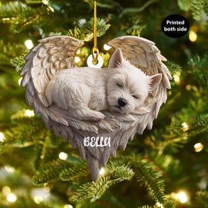 May include: A white puppy ornament with angel wings, suspended by a gold string. The puppy rests in the wings' centre, with the name "BELLA" below. The text "Printed both side" is in a black circle.