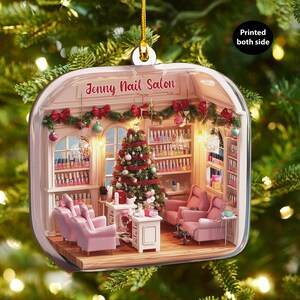 May include: A Christmas ornament featuring a miniature nail salon scene. The ornament has a clear, rounded shape with a detailed interior, including pink chairs, a Christmas tree, and shelves of nail polish. The text "Jenny Nail Salon" is visible.