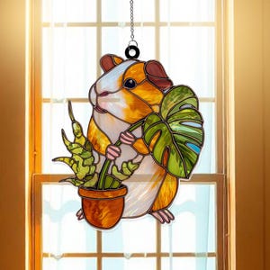 May include: Stained glass window hanging featuring a guinea pig holding a potted plant and a large leaf. The guinea pig has orange, white, and brown fur. The plant has green leaves and a brown pot. A black chain is attached for hanging.