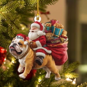 Pu&ograve; includere: Ornamento natalizio con Babbo Natale a cavallo di un bulldog. Babbo Natale indossa un abito e un cappello rossi, e il bulldog ha un cappello con la scritta "Bella". Un grande sacco rosso pieno di regali &egrave; dietro Babbo Natale. L'ornamento &egrave; appeso a un filo d'oro.